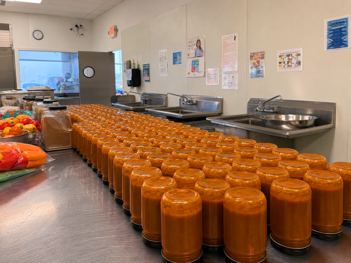 Rows of unlabeled Smoky Bell sauce jars inverted after hot filling in a commercial kitchen.